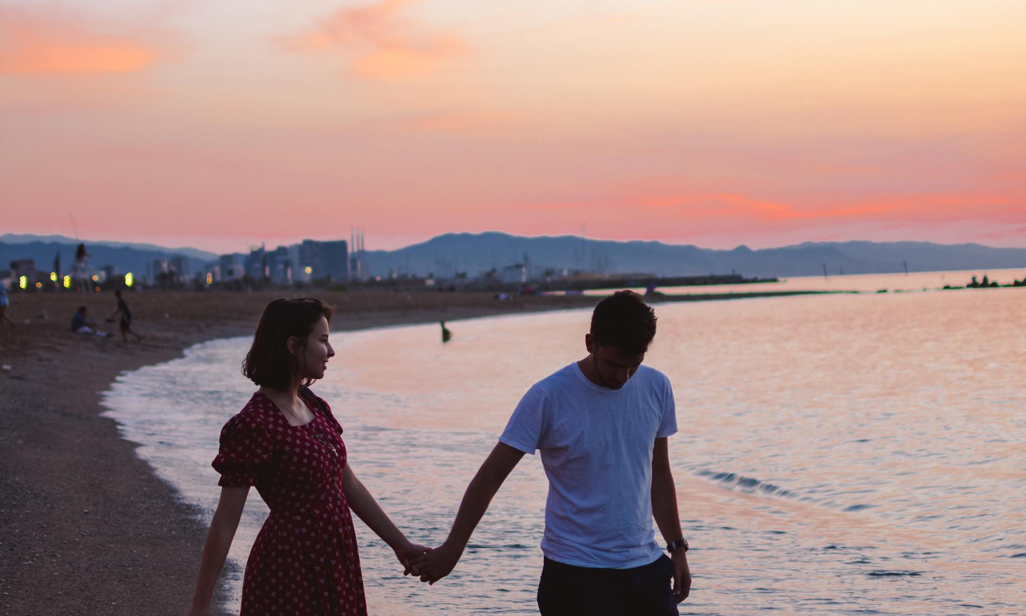 Photo by Theodore Vasile showing the beach (La Barceloneta) in Barcelona (Catalunya, Spain). A couple stroll along the beach holding hands.
